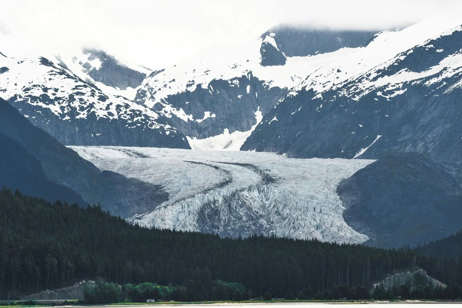 Stunning Alaska landscape with snow-capped mountains, lush forests, and a winding river under a crisp blue sky.