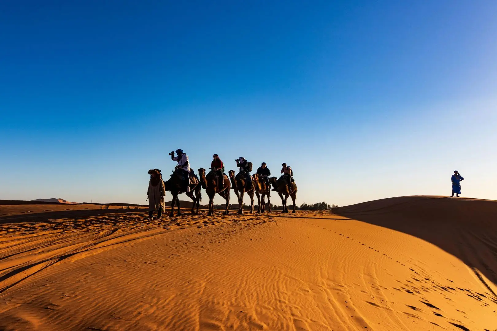 Vast golden dunes of the Sahara Desert in Morocco, with rippling sand patterns under a clear blue sky.